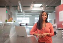 woman in orange long sleeve shirt sitting beside table with macbook pro