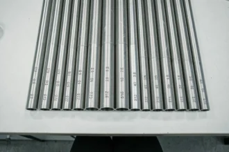 Tubes inox de différents diamètres pour plomberie alignés sur un établi blanc, vue de dessus