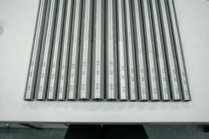 Tubes inox de différents diamètres pour plomberie alignés sur un établi blanc, vue de dessus